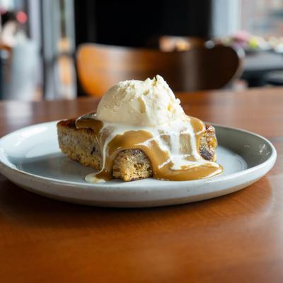 Sticky Toffee Pudding on a white plate with vanilla ice cream.