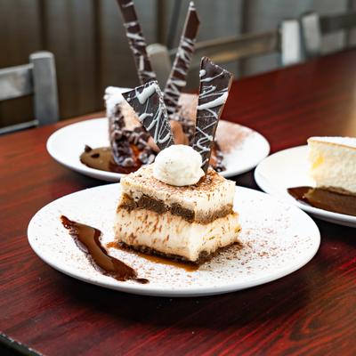 Tiramisu, chocolate espresso cake, and cheesecake on a dark wooden table.