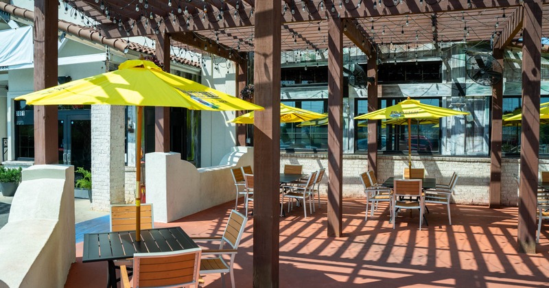 Outdoor dining area with tables, chairs, parasols and a wooden pergola