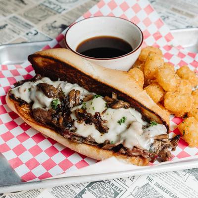 Grilled beef and mushroom sandwich with melted cheese, dipping sauce, and tater tots.