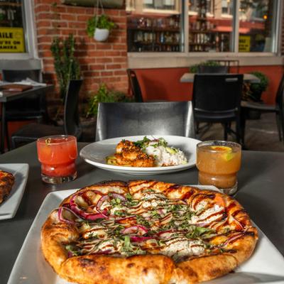 Wood-fired pizza with cocktails and rice dish served on a patio table.