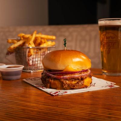 Chili cheeseburger with fries, beer, and ketchup in the background.