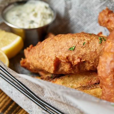 Fried fish fillet served with thick potato fries, tartar sauce, and lemon wedges.