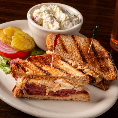 Reuben sandwich, served with lettuce, tomato, onion, pickles, and potato salad.