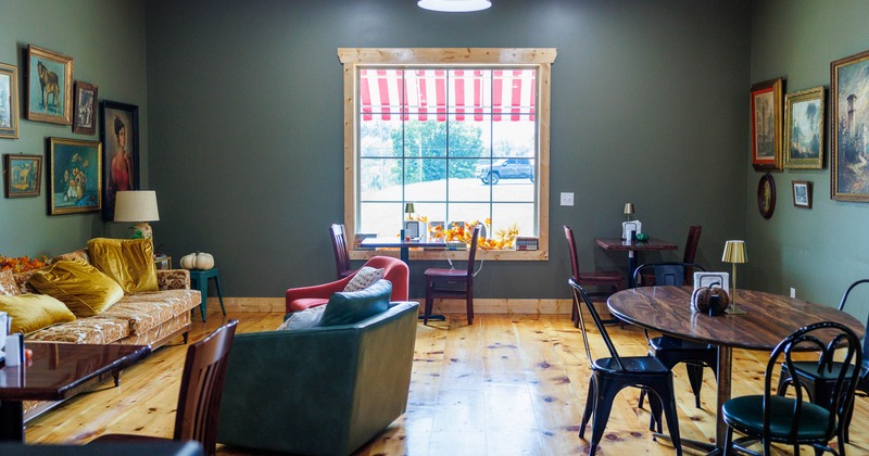 Warmly lit interior - green walls, wood floors, framed artwork, sofas, tables, chairs.