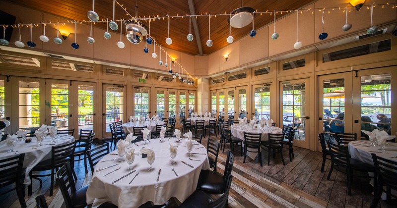 Indoor dining area with tables set for an event, decorated with hanging orbs and fairy lights