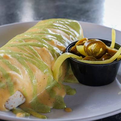 Burrito topped with sauce, served with pickled jalapenos.
