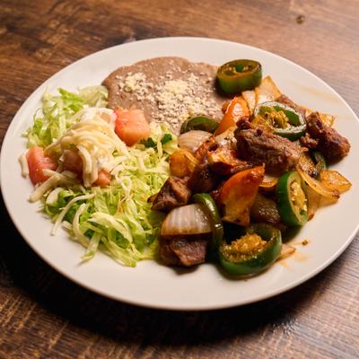 Mexican beef steak with vegetables, refried beans, and shredded lettuce.