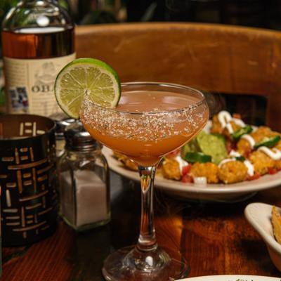 Mystic Paloma cocktail served alongside bottle of whiskey and a plate of loaded tots.