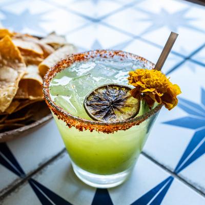 Cucumber Margarita sits on a tile table next to tortilla chips.