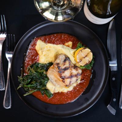 Chilean sea bass plate on a black table with white wine and utensils on the side, top view.