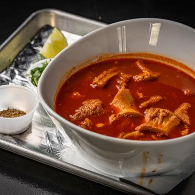 A bowl of menudo on a metal tray with condiments.