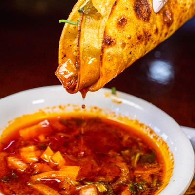 Crispy folded taco dripping red consommé.