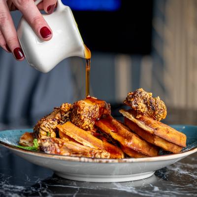 Syrup being poured over fried chicken and waffles.