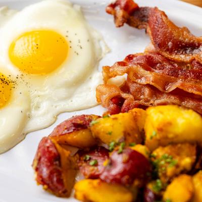 Breakfast plate with two sunny side up eggs, home potatoes, and crispy bacon.