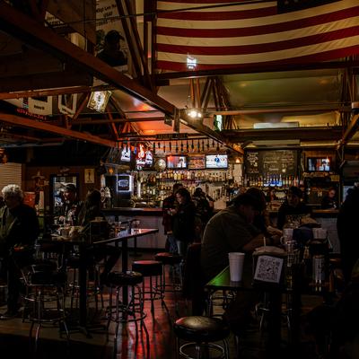 Interior with tables, chairs, guests, bar, and wall-mounted TVs.
