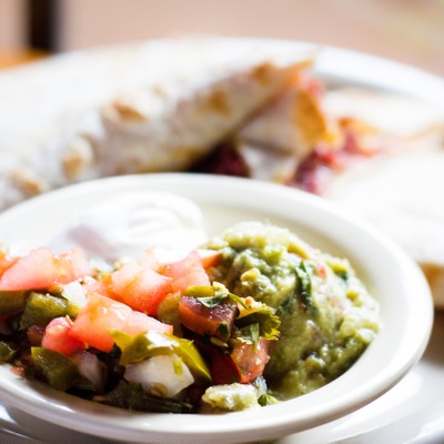 Quesadilla stuffed with corned beef on a plate served with a dish that contains guacamole, sour cream and pico de gallo