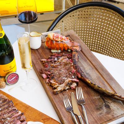 Sliced grilled steak and lobster served on a wooden board with wine and sides.