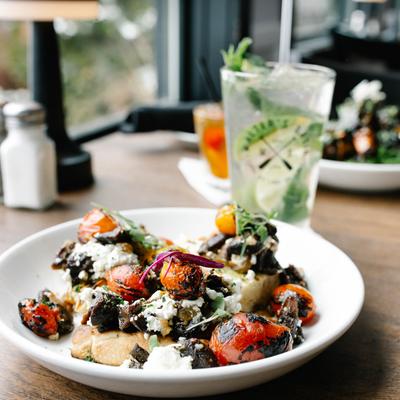 A plate with bruschetta on a table, with a glass of mojito and blurred food  by a window.