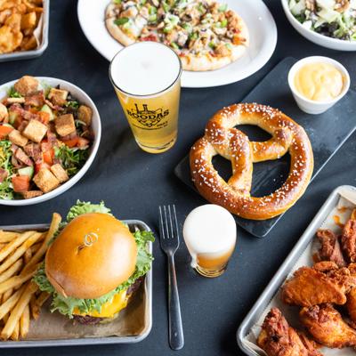 A burger with fries, a large pretzel, chicken wings, a pizza, salads, and glasses of beer.