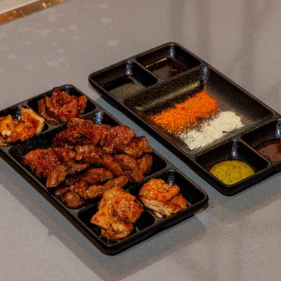 Takeout trays filled with Korean fried chicken and side dishes.