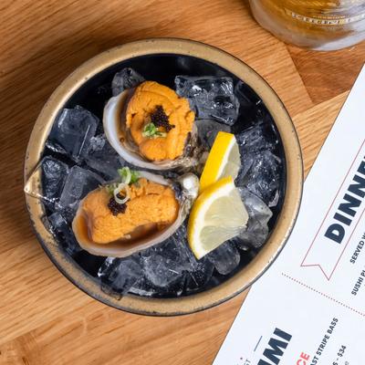 Two oysters topped with sea urchin served on ice in a bowl.
