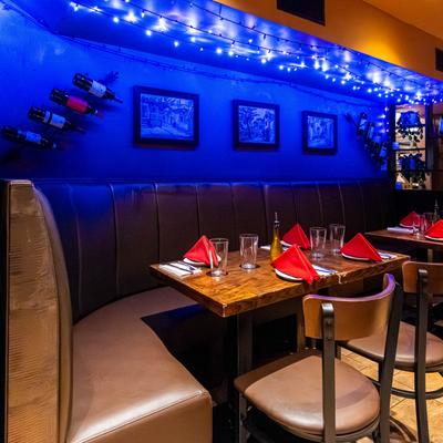 A restaurant booth with blue mood lighting, wine bottles on the wall, and tables set for dining.