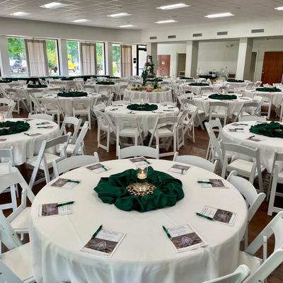 Event venue with round tables, white linens, and green decorations.