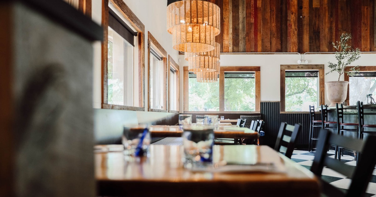 Bright restaurant interior with wooden tables, black chairs, and woven pendant lights