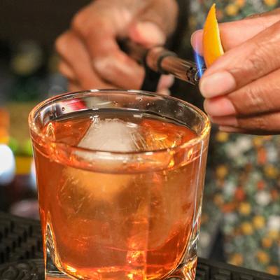 Old Fashioned glass being decorated with flamed lemon peel.