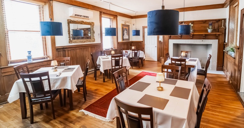Interior, dining area, white cloth tables for four, ready for guests, fireplace in the back