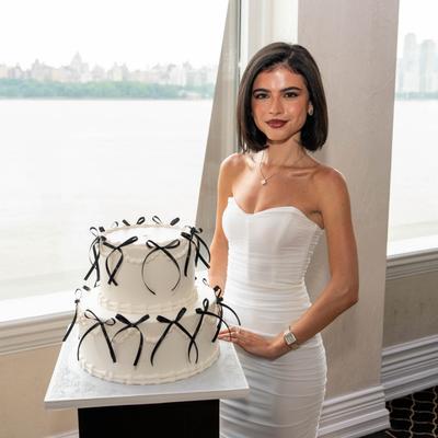 Person in white dress holding ribbon a decorated cake.