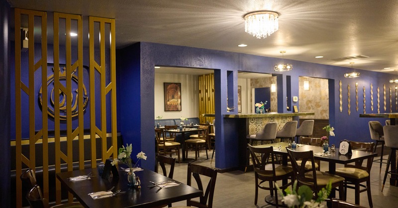 Modern restaurant interior with blue walls, gold decor, and a bar area