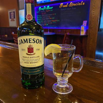 A bottle of Irish whisky alongside a glass of drink garnished with a lemon wedge and a straw.