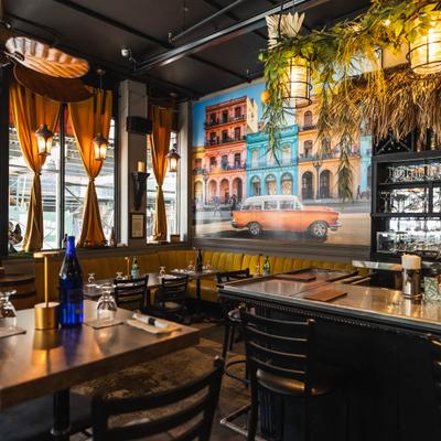 Restaurant interior with a bar, banquette seating, and a colorful mural.