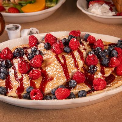 Three pancakes topped with blueberries and raspberries.
