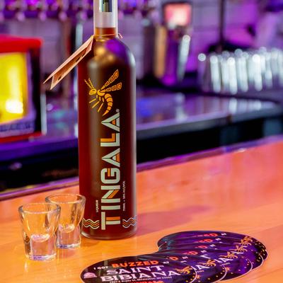 A bottle of liqueur with two empty shots and coasters on a bar counter.
