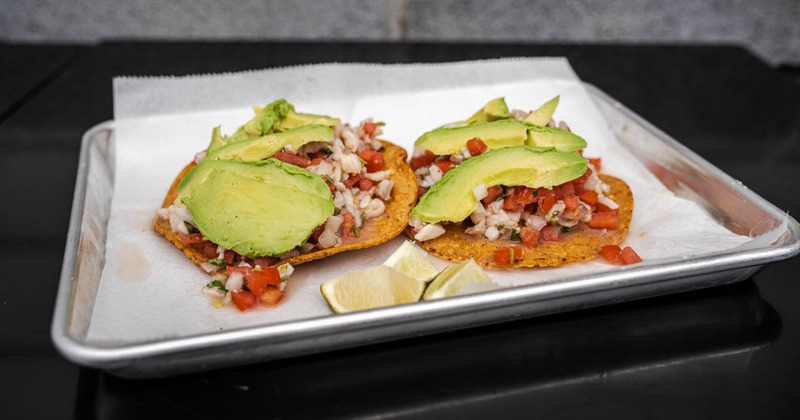 Tostada ceviche topped with avocado slices and served on a tray