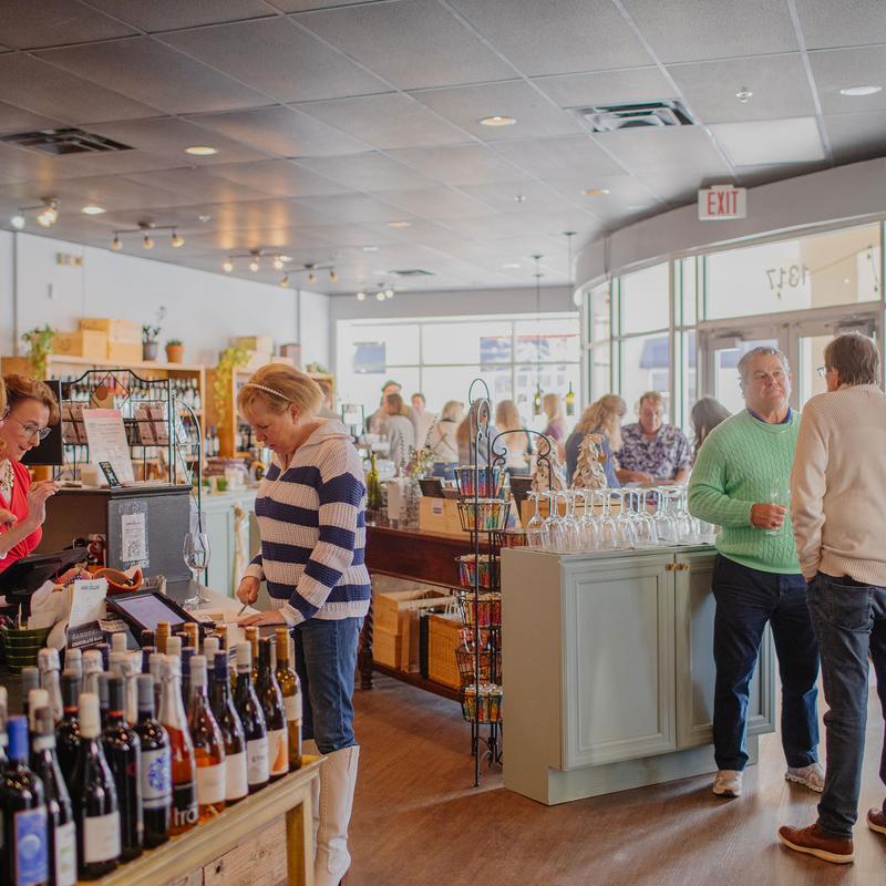 Interior of a wine shop filled with people browsing bottles and socializing.