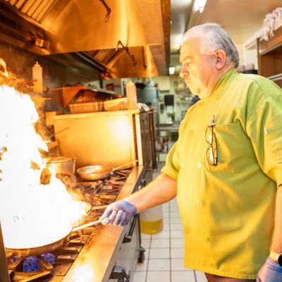 Chef preparing food with a large flare-up of fire on the stove.