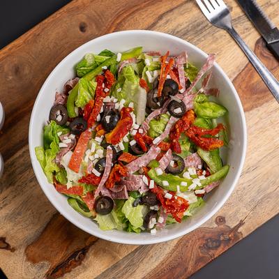 Bowl of Antipasti Salad served on a wooden board.