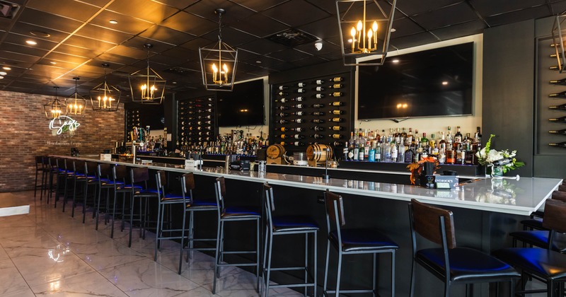 Modern bar interior with a long marble countertop, high stools, and pendant lights