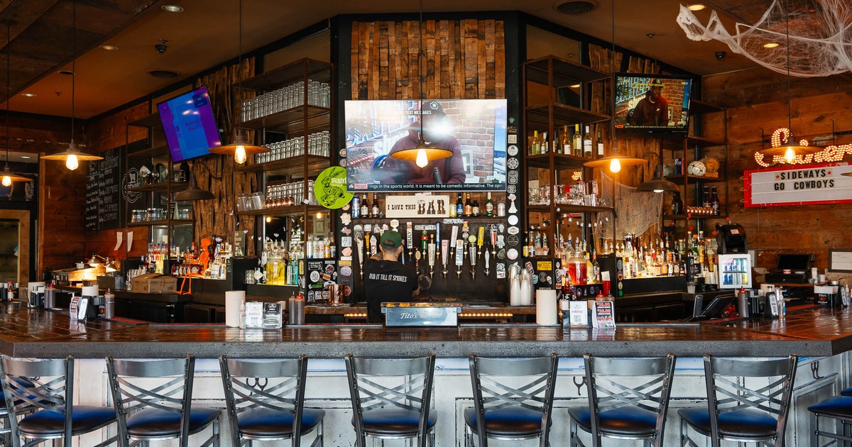 Interior,  a fully stocked wooden bar with several empty bar stools in the foreground