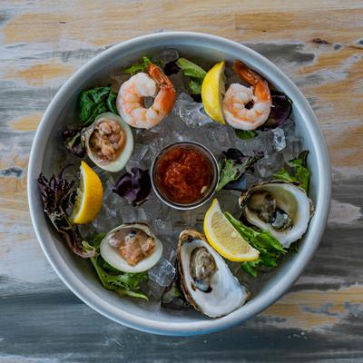 Chilled seafood platter with shrimp, oysters, clams, lemon wedges, and cocktail sauce.