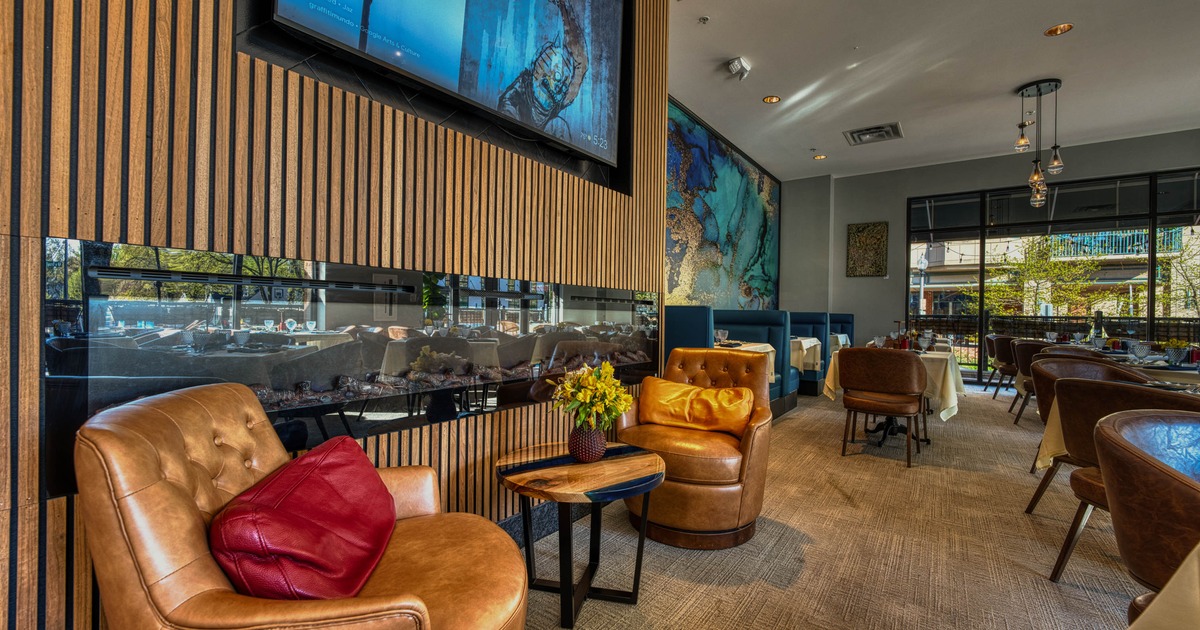Elegant restaurant interior with leather armchairs, a television and dining areas.