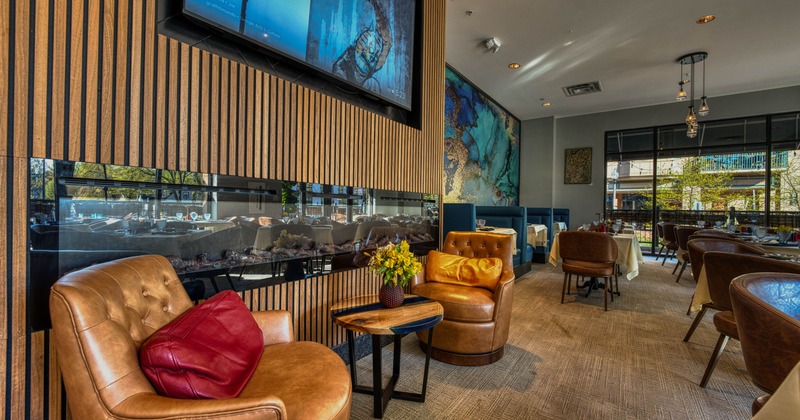 Elegant restaurant interior with leather armchairs, a television and dining areas.