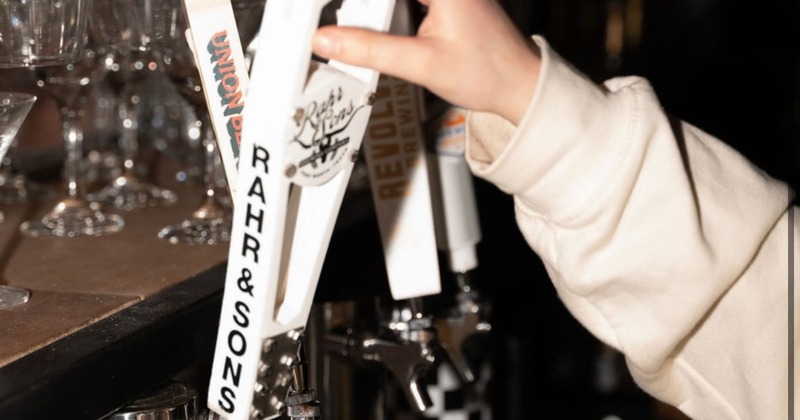 A person at a bar pouring a draft beer using one of several tap handles
