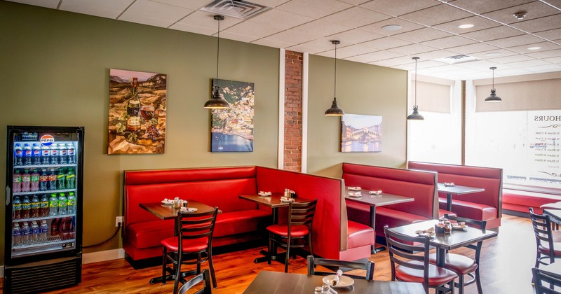 Dining area with red booths, wooden tables, chairs, pendant lamps and a beverage cooler