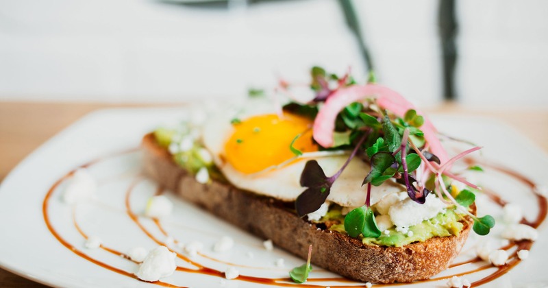 Avocado toast topped with goat cheese, fried egg and micro-greens
