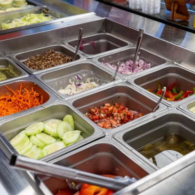 Salad bar filled with fresh chopped vegetables in metal containers.